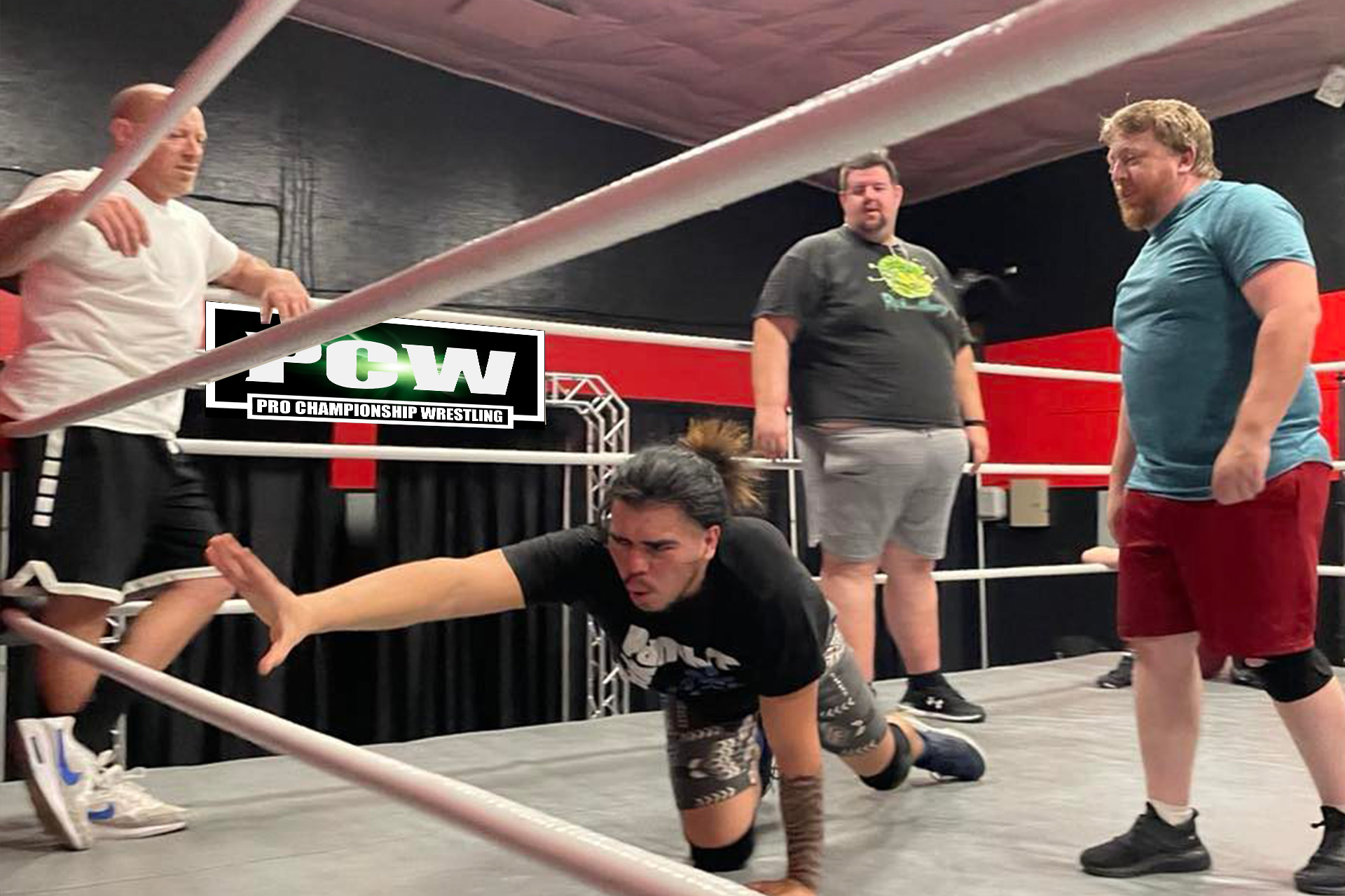 A determined young PrimeTime University student desperately reaches for the bottom rope as Coach Zack 'PrimeTime' Reeb, Bad News Blakeslee, and referee Jimmy Mac watch intently during a PCW training session